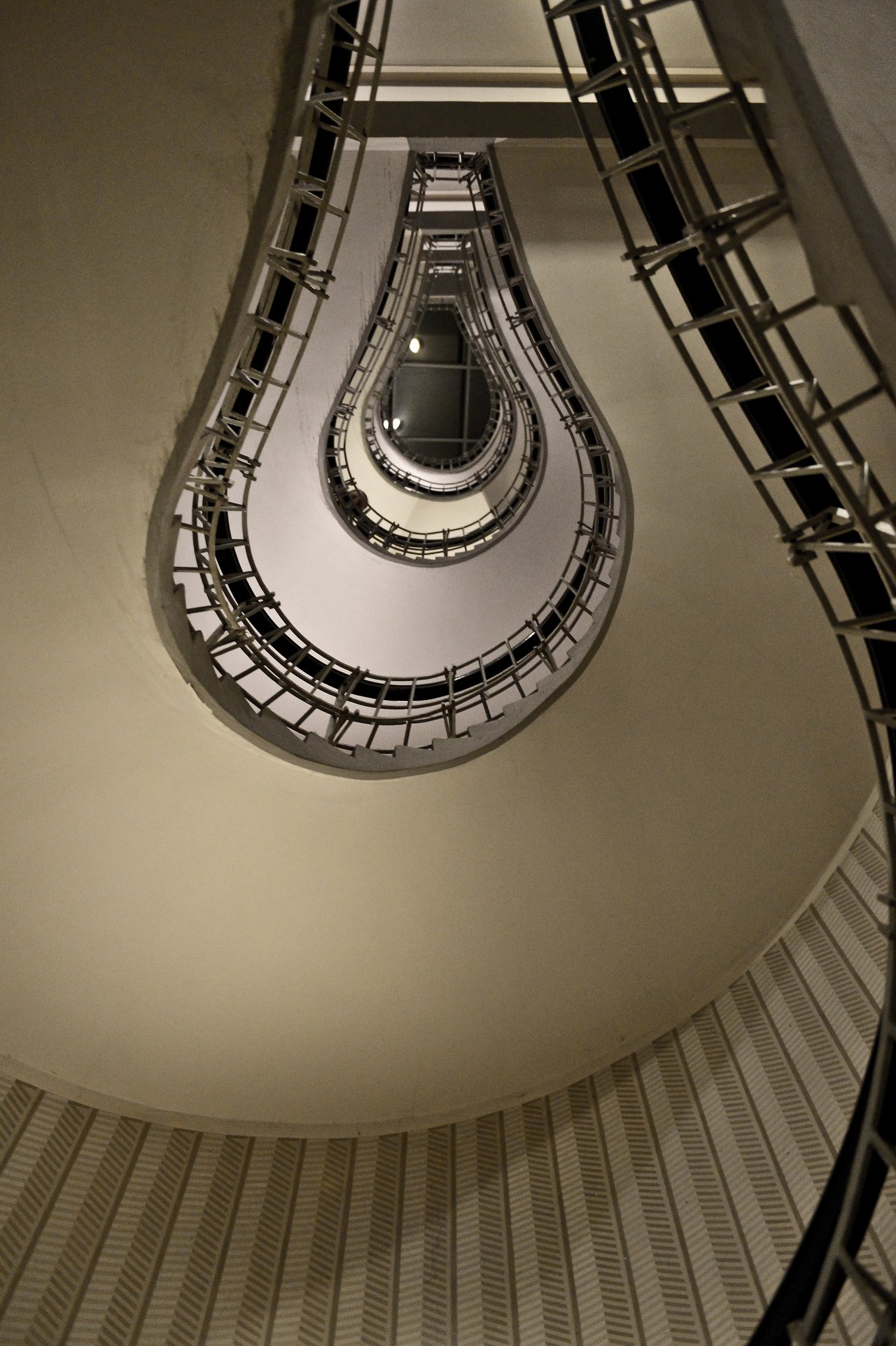 Looking up at a spiral staircase with metal railings, forming a lightbulb-shaped pattern in the center.