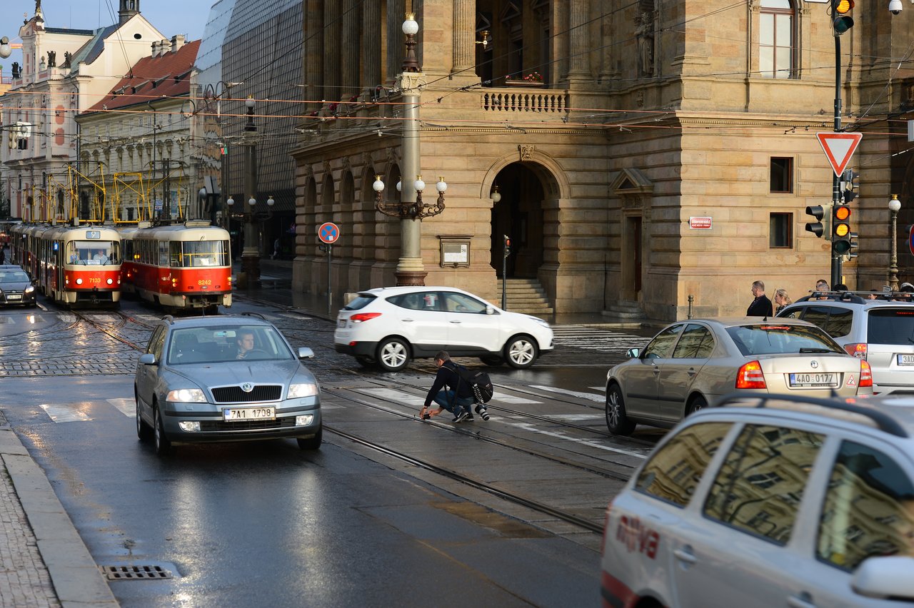 A person in a wheelchair has fallen on tram tracks in a busy intersection as cars and trams approach.