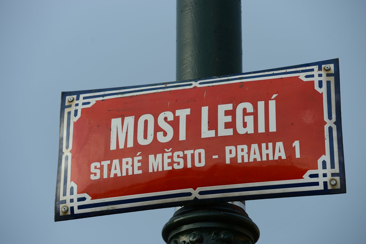 A red street sign on a green pole in Prague.