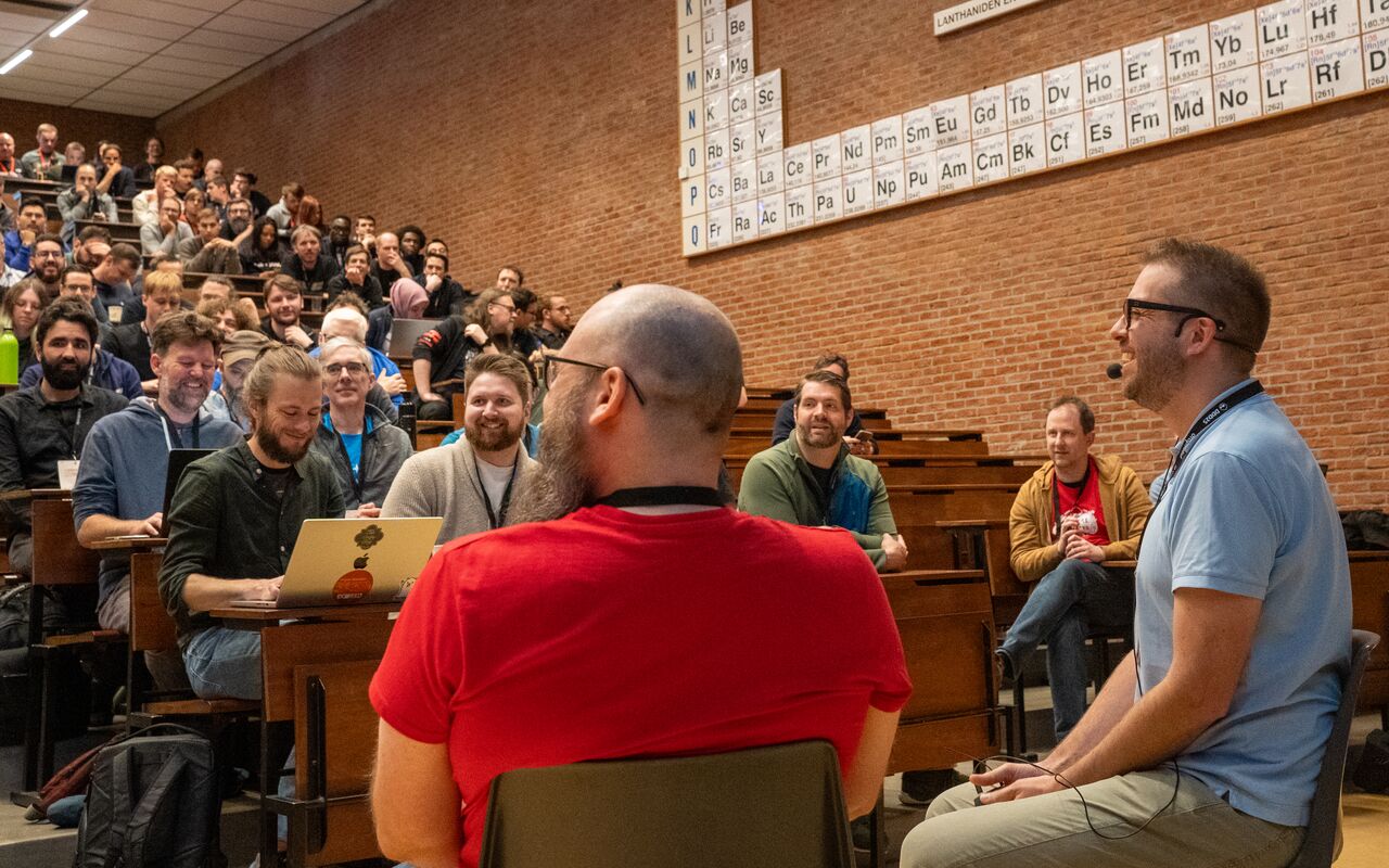 Dries Buytaert speaking during a Q&amp;A session at Drupal Dev Days Leuven, facing a large, engaged audience seated in a university lecture hall.