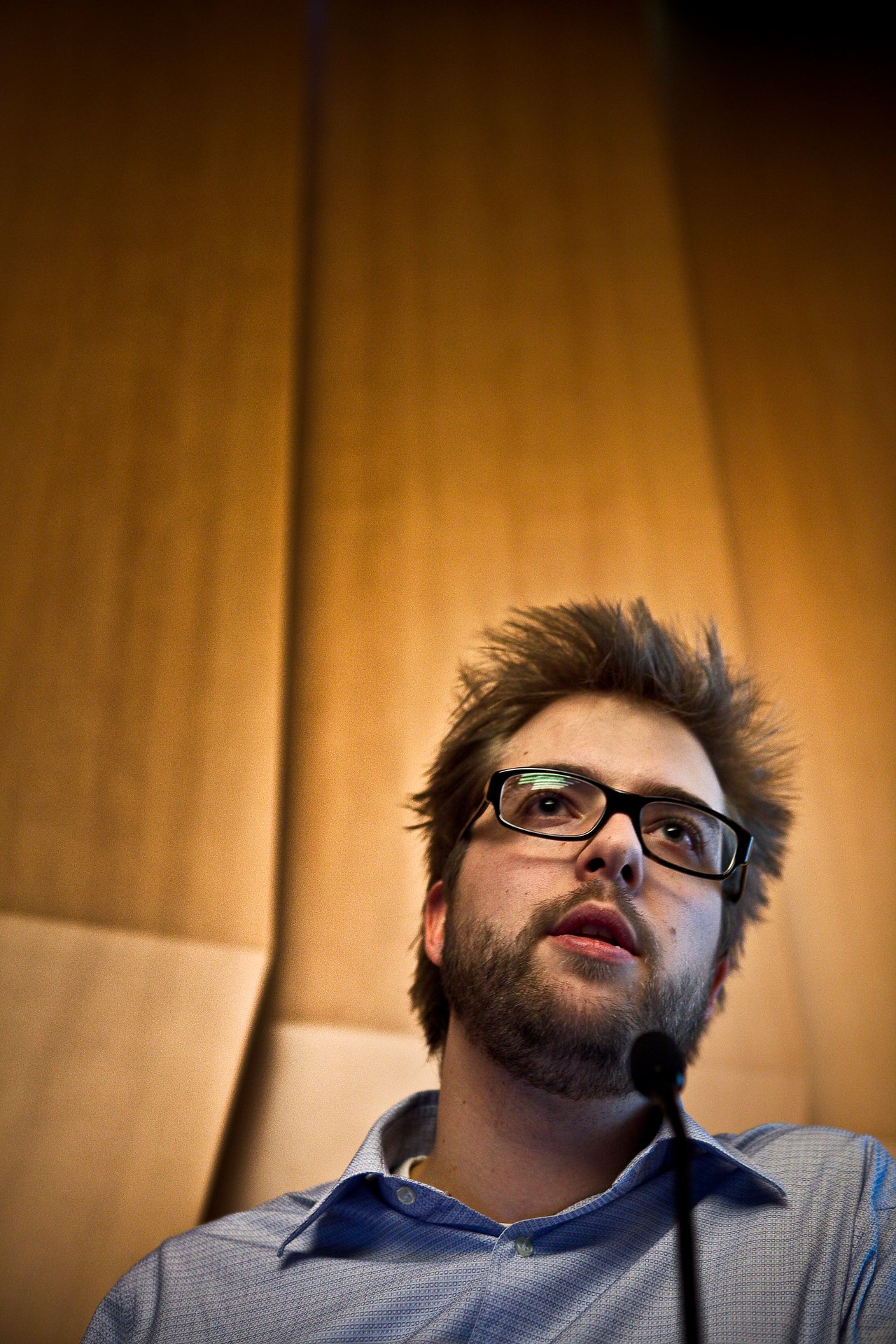 A man in glasses and a blue shirt speaks into a microphone during a presentation.