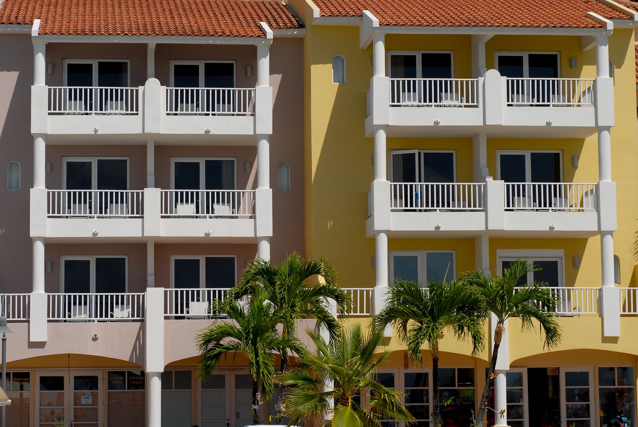A colorful hotel building with balconies, white railings, and palm trees in front.