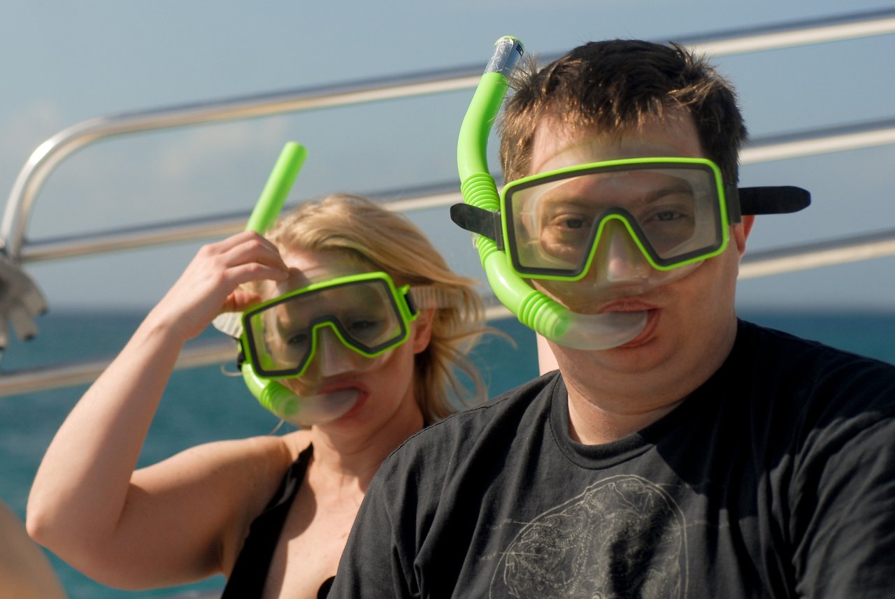 Two people wearing snorkel masks sit on a boat, preparing for snorkeling in the ocean.