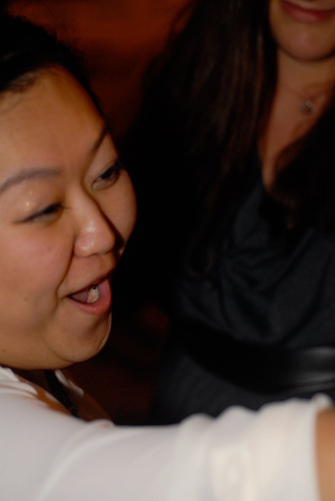 A woman smiling and enjoying a party, with another person partially visible in the background.