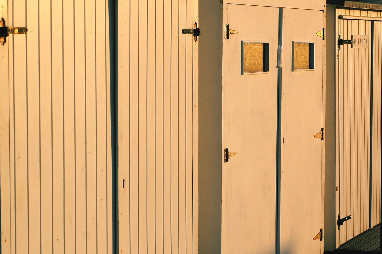 A row of wooden cabin doors with metal hinges, some featuring small windows, illuminated by warm sunlight.