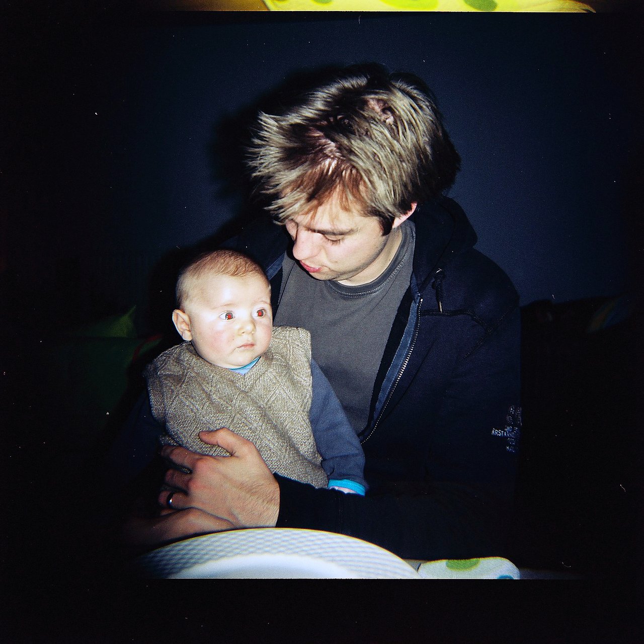 A man holds a baby in his arms, looking down while the baby gazes off to the side.