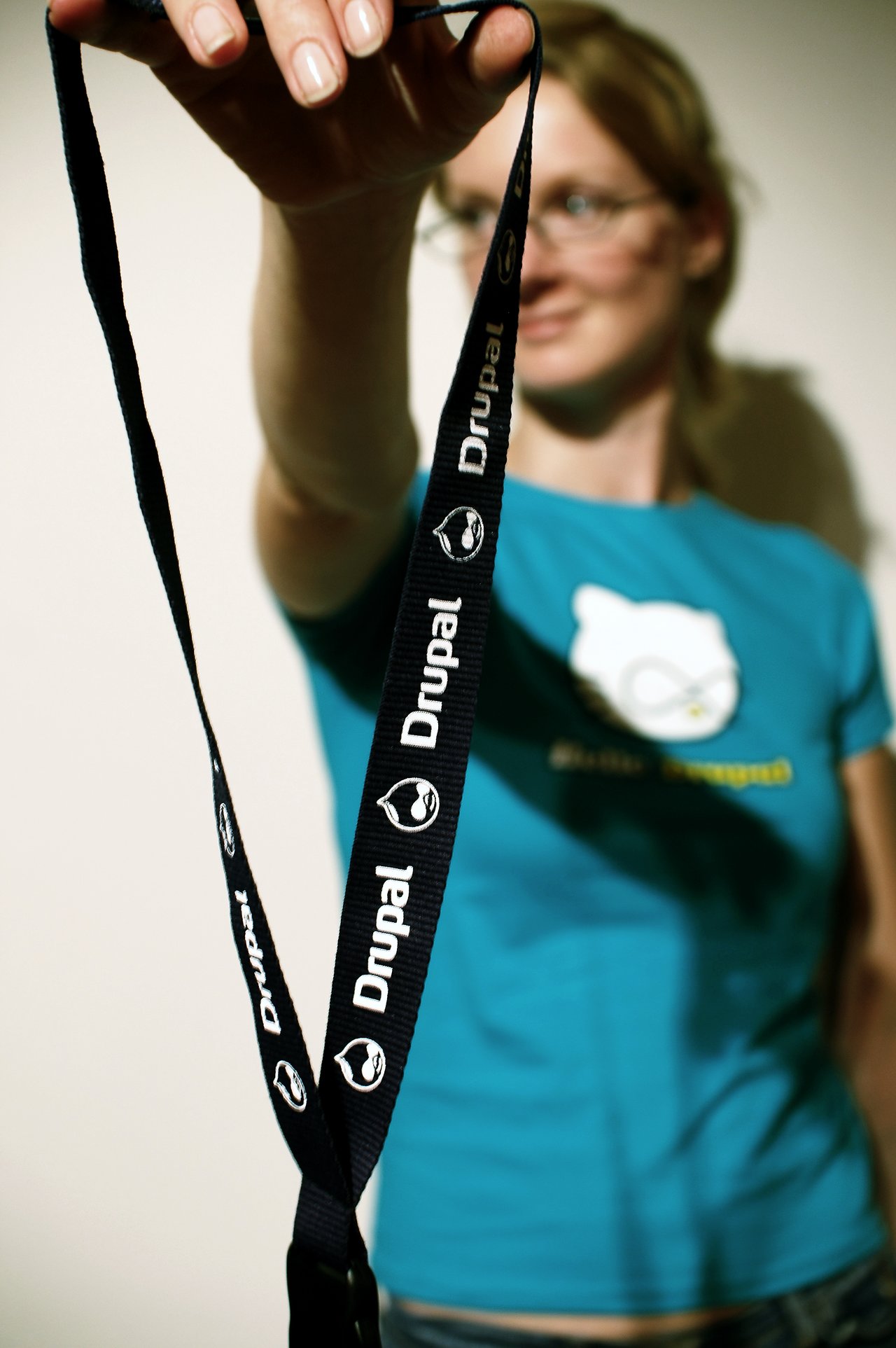 A person in a blue shirt holds out a black Drupal-branded lanyard toward the camera.