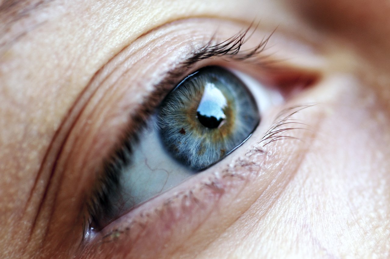Close-up of a human eye with a mix of blue and green colors, reflecting light.