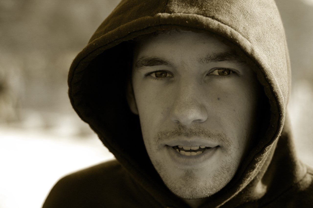 A person wearing a hooded sweatshirt looks directly at the camera with a slight smile.