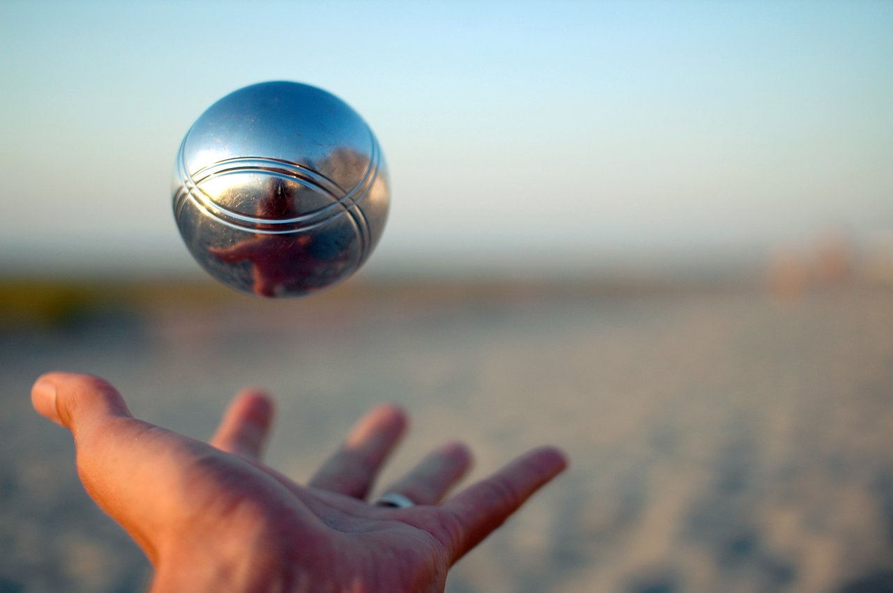A hand tosses a shiny metal ball into the air, reflecting the surroundings on its surface.
