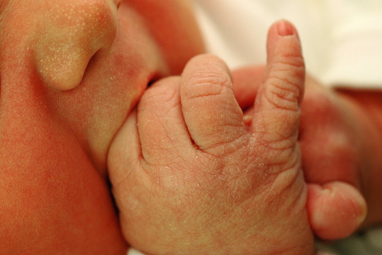 A newborn baby sucking on their tiny hand, with small fingers and wrinkled skin visible up close.