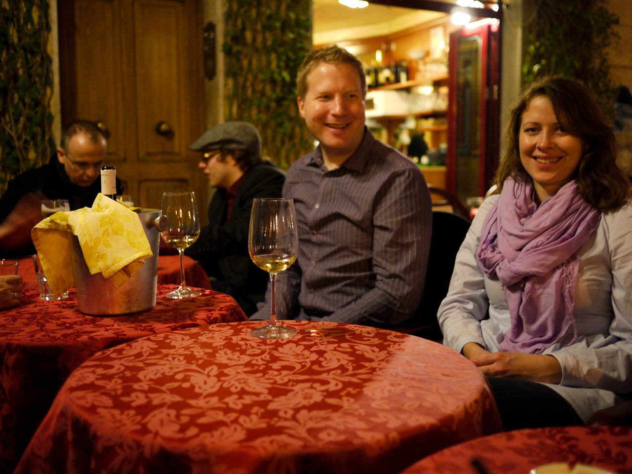 Two people sit at a restaurant table with wine glasses, smiling.