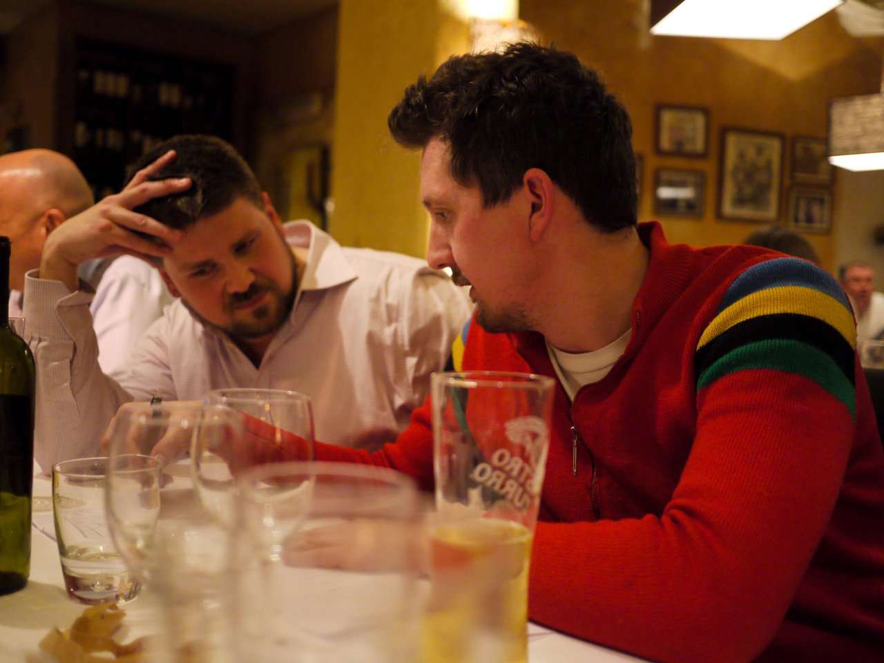 Two men sit at a restaurant table, engaged in a conversation.