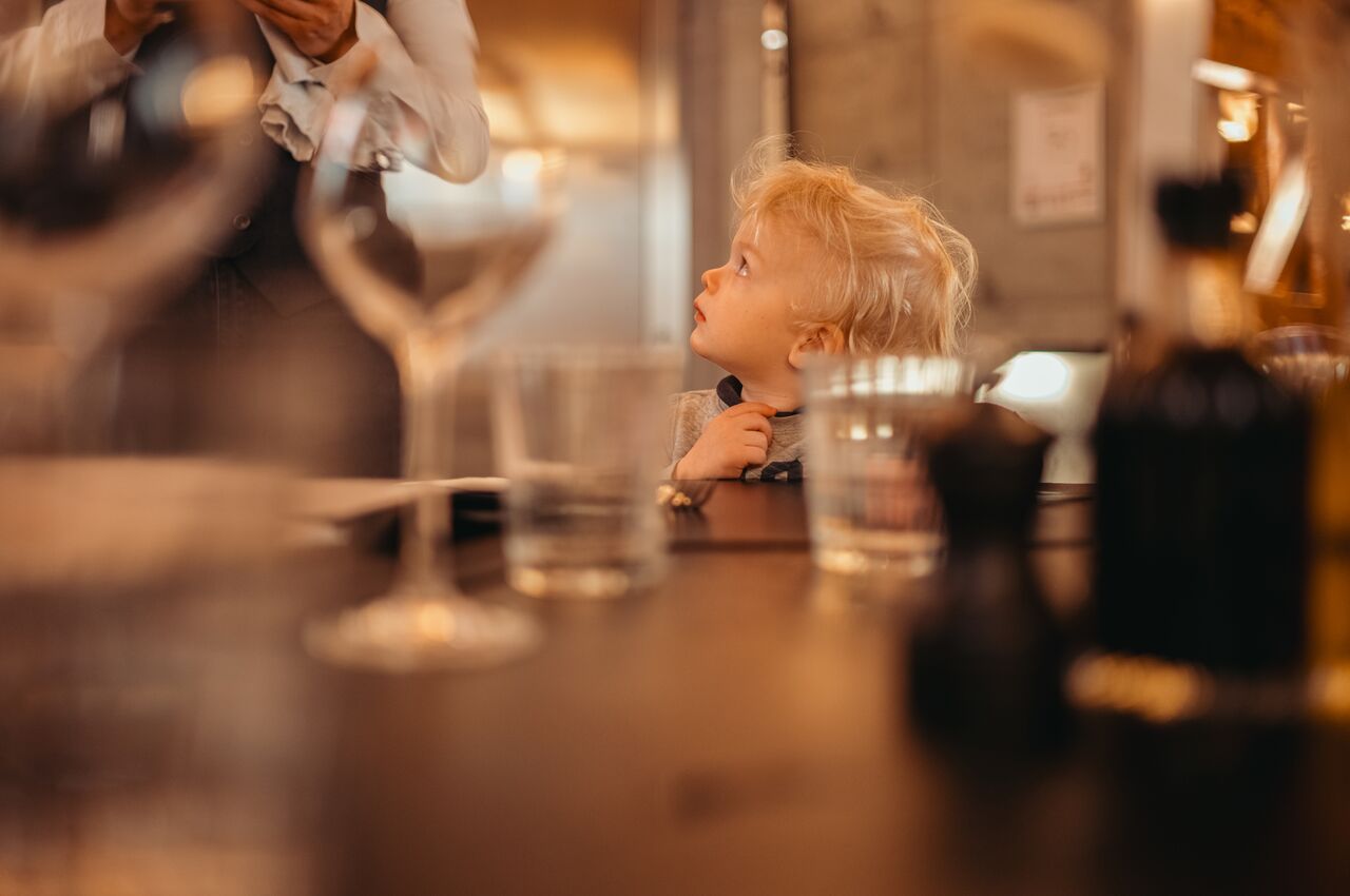 A young toddler with blond hair gazes upward in wonder at a waitress.