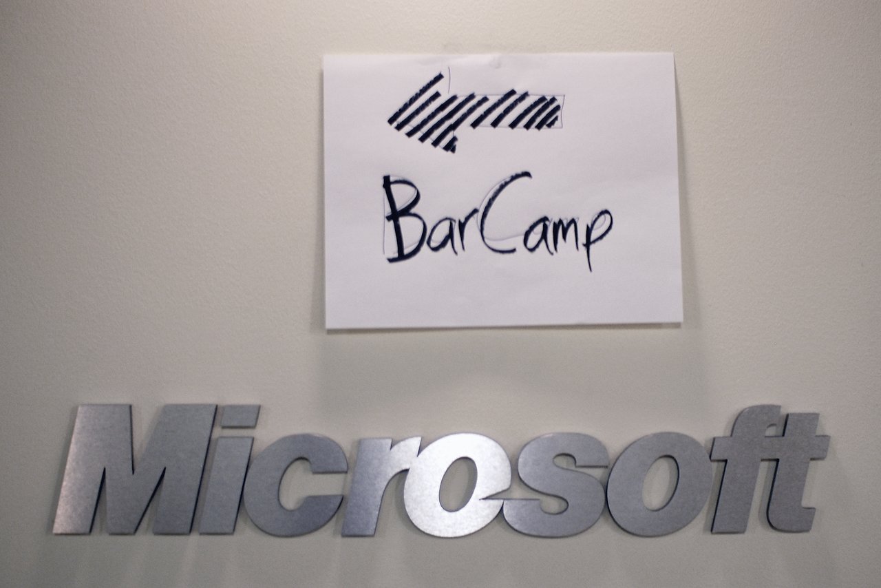 A handwritten sign with an arrow directs attendees to BarCamp above a Microsoft logo on a wall.