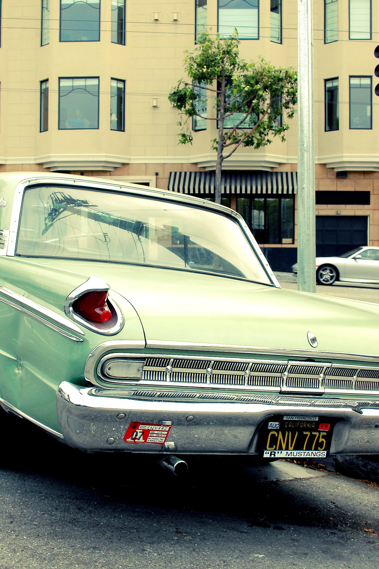A vintage green Buick is parked on a city street, showing its rear design, chrome details, and tail lights.