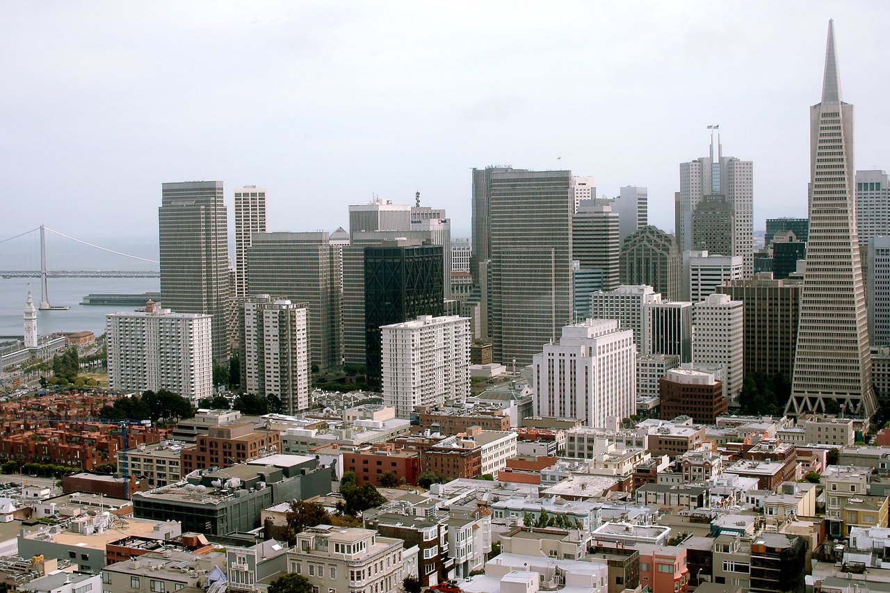 A view of downtown San Francisco with tall buildings, including the Transamerica Pyramid, and the Bay Bridge in the background.