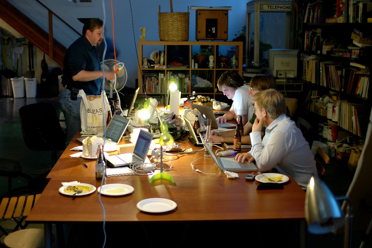 People working on laptops at a table with food and drinks in a shared workspace.