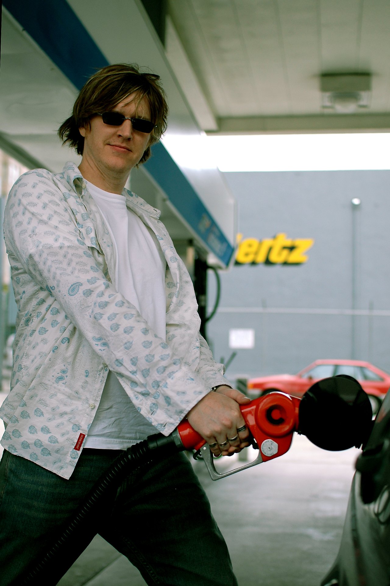 A person wearing sunglasses pumps gas into a car at a fuel station.