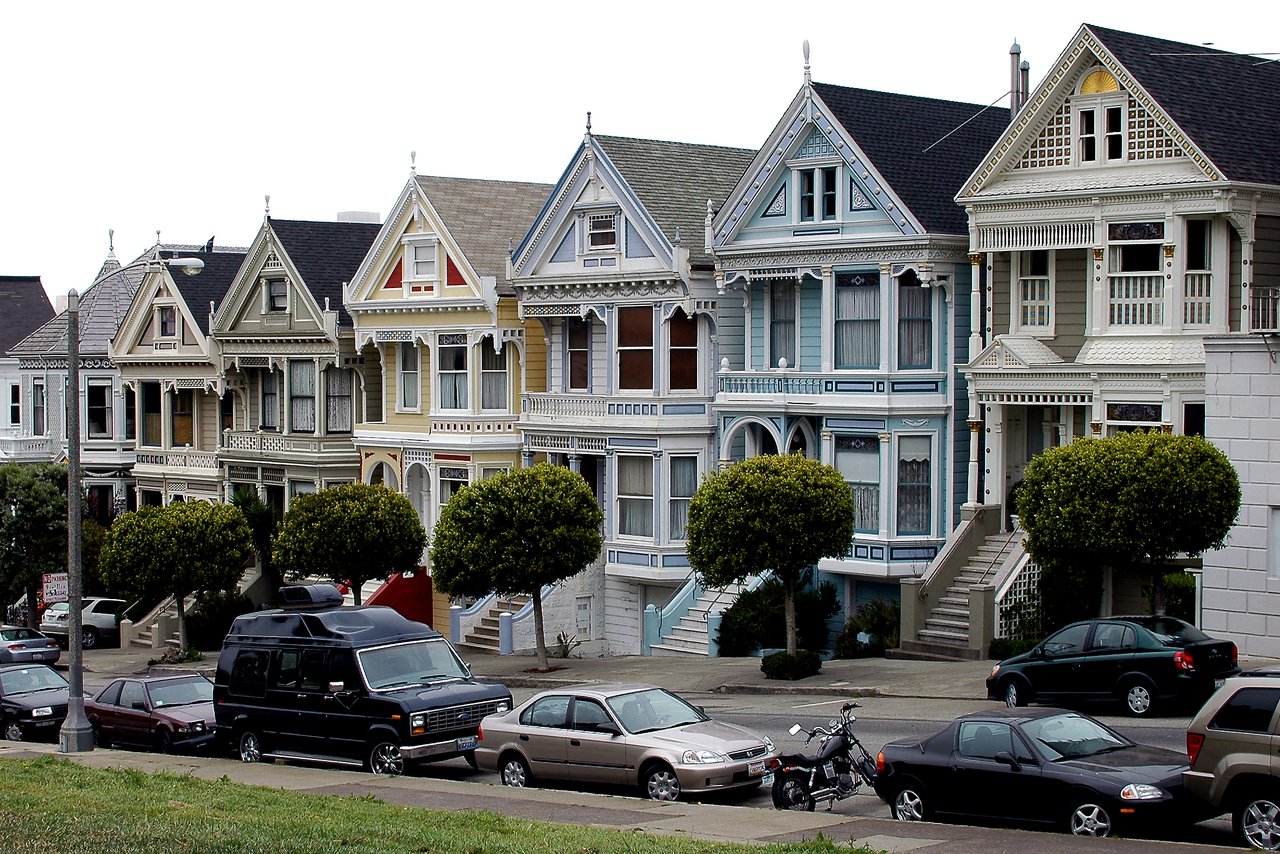 A row of colorful Victorian houses, known as the Painted Ladies, with parked cars in front.