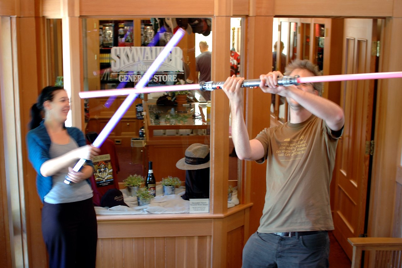 Two people playfully duel with toy lightsabers indoors, crossing their glowing blades while smiling and having fun.