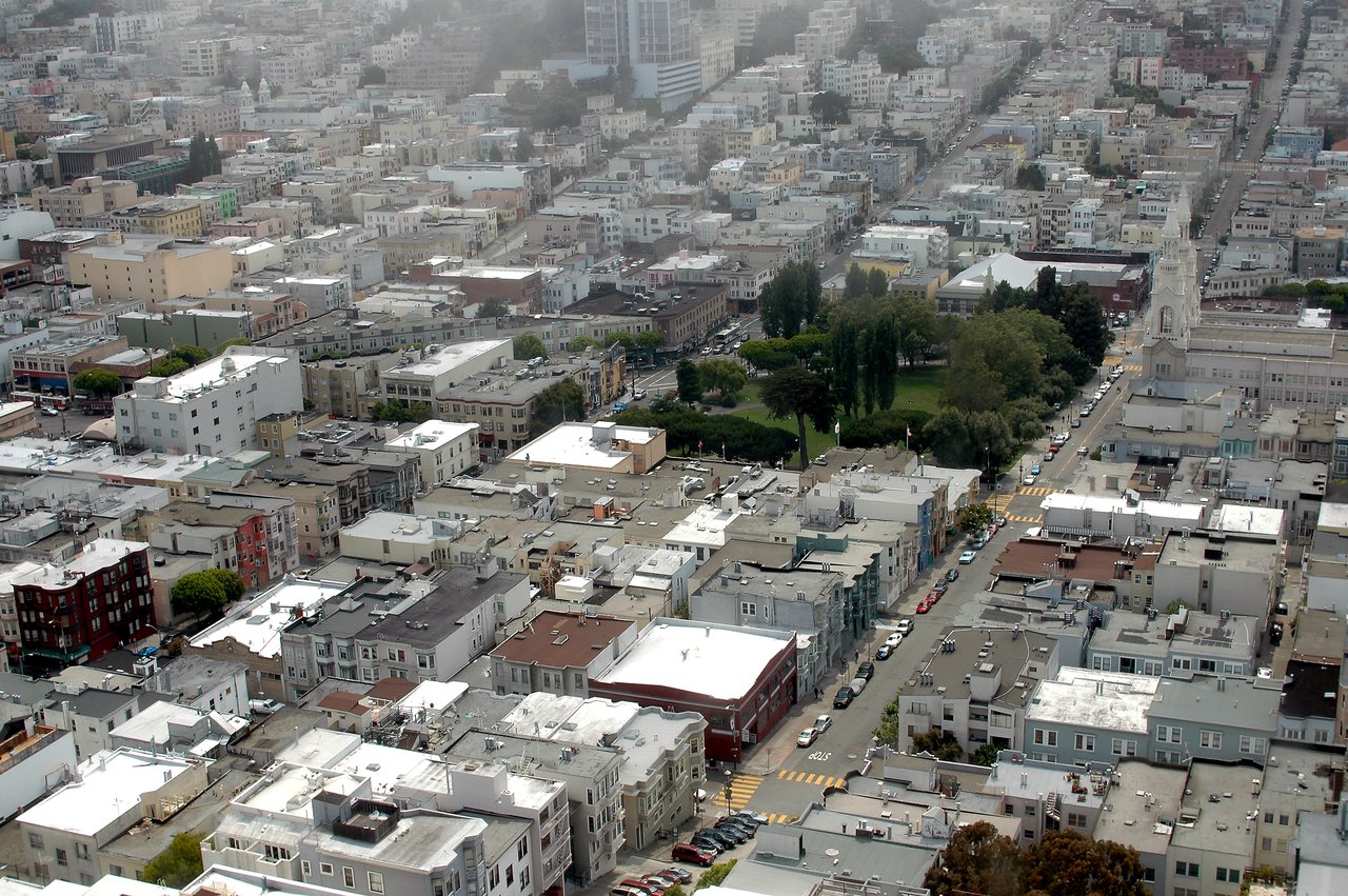 Aerial view of a dense urban neighborhood with tightly packed buildings, streets, and a small park in the center.