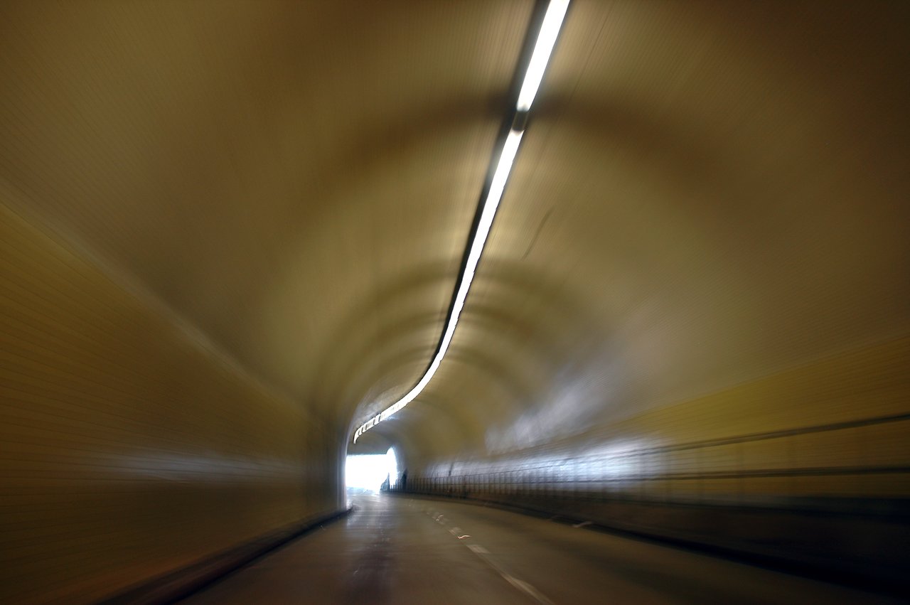A blurry view of a tunnel with a curved ceiling, a central light strip, and a bright exit ahead.