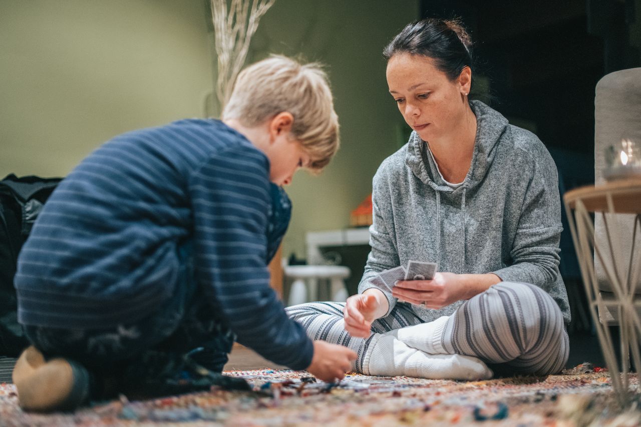 A woman and a child sit on the floor, playing cards together in a relaxed setting.
