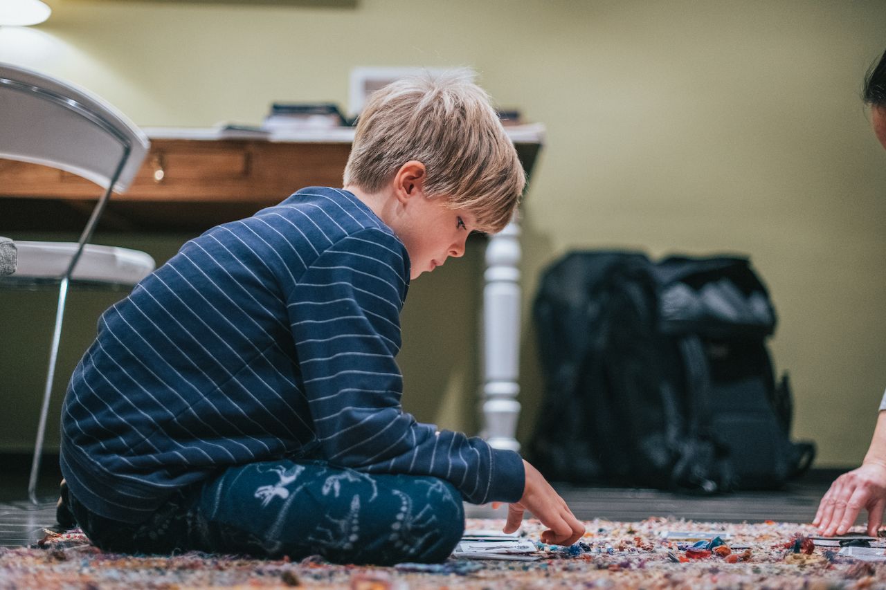 A child sits on the floor, focused on playing a card game with another person.
