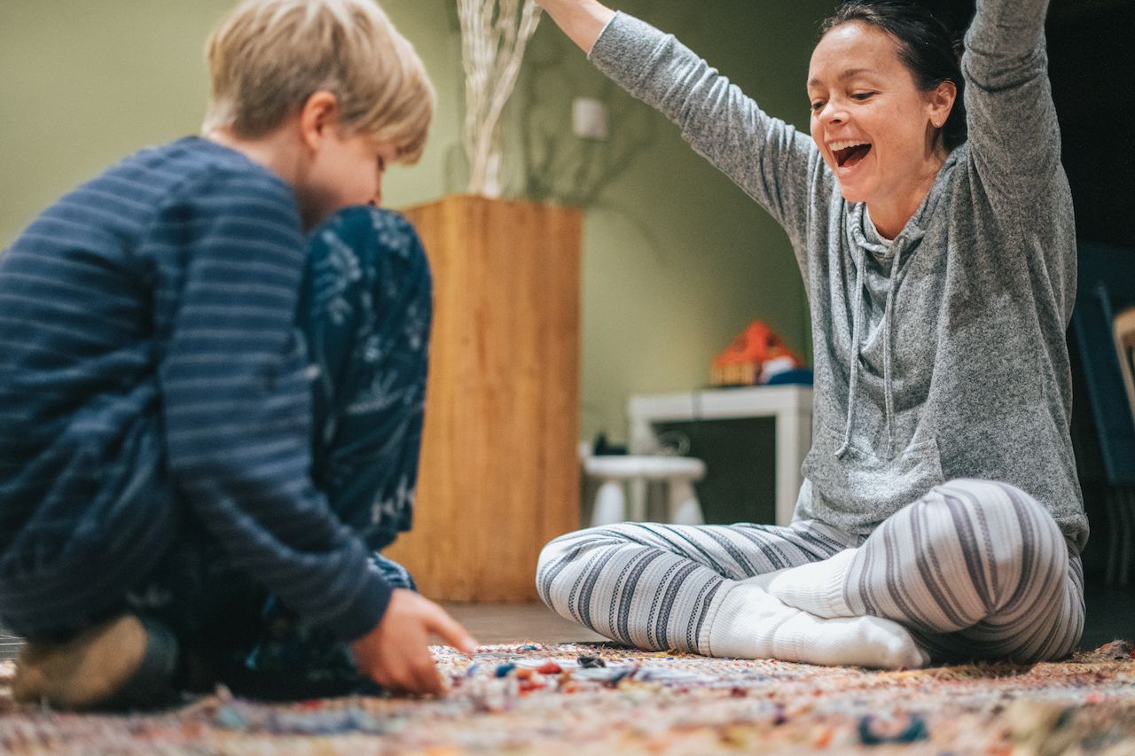 A child and an adult sit on the floor playing cards.