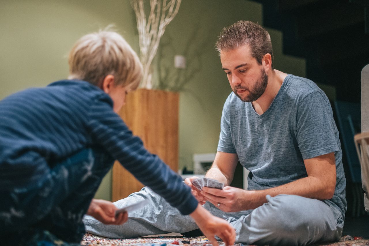 A child and an adult sit on the floor, playing a card game together and focusing on their moves.