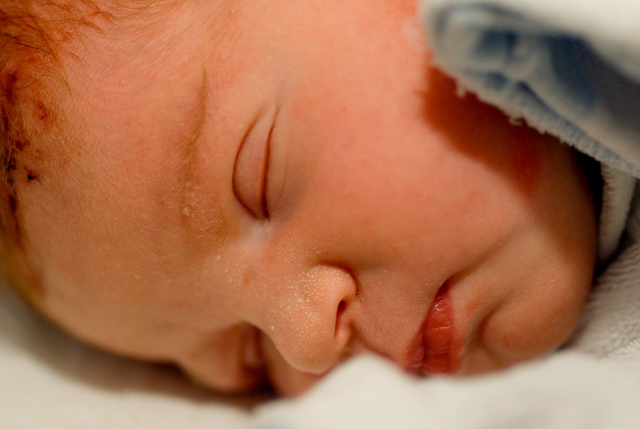 Close-up of a newborn baby sleeping, wrapped in a soft blanket with eyes closed and lips slightly parted.