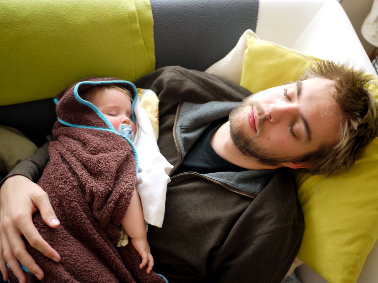 A man and a baby are sleeping on a couch.