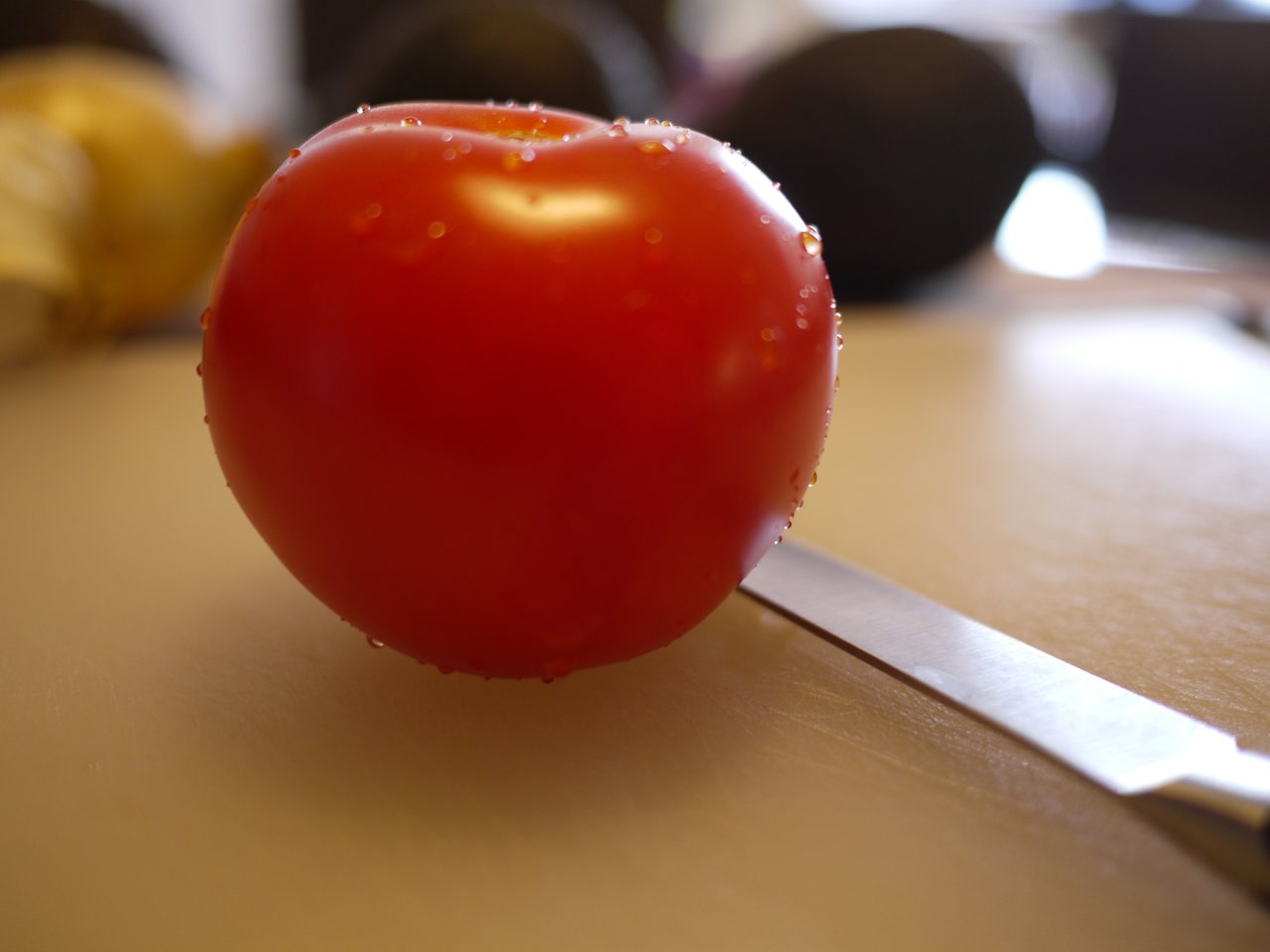A fresh red tomato with water droplets rests on a cutting board beside a knife.