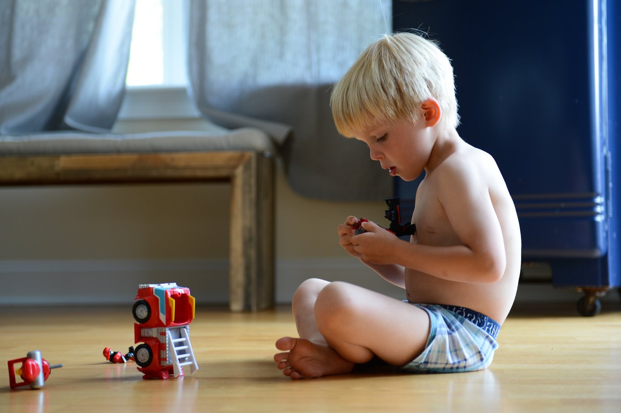 A young child sits on the floor, focused on assembling a small toy fire truck with scattered pieces nearby.