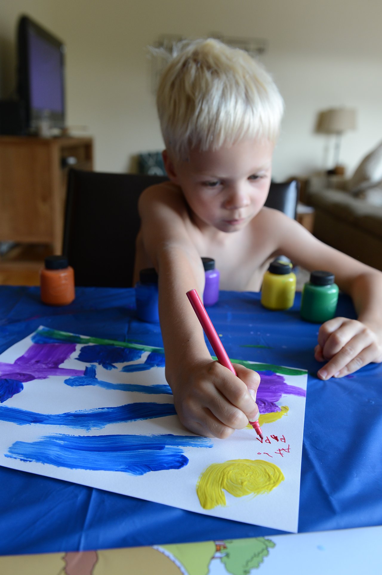 A young child paints on paper with bright colors, holding a red pencil and focusing on their artwork.