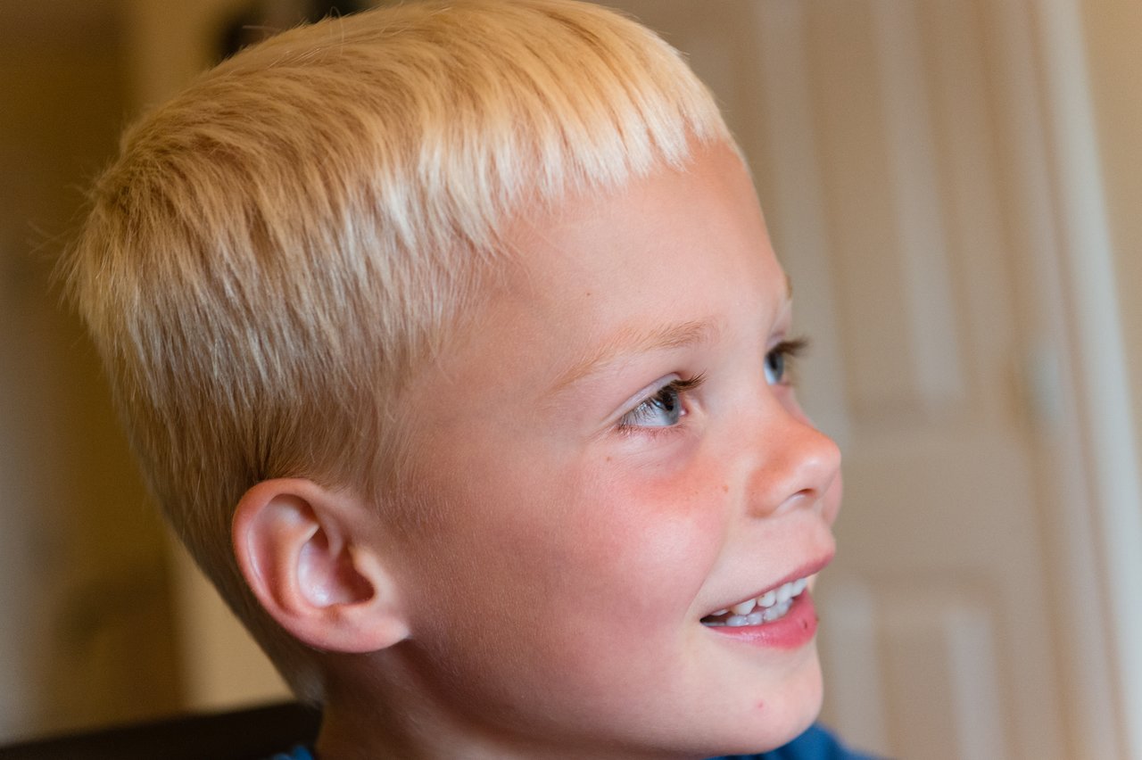A young child with short blond hair laughs while looking to the side.