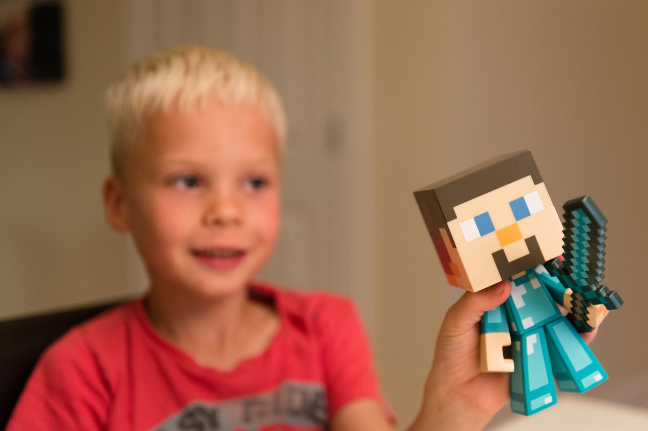 A child in a red shirt holds a Minecraft toy figure with a sword, smiling during a birthday celebration.