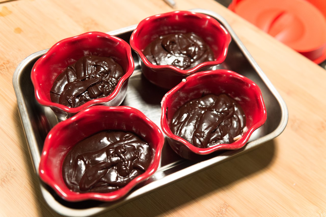 Four red ramekins filled with chocolate batter sit on a metal tray, ready for baking.