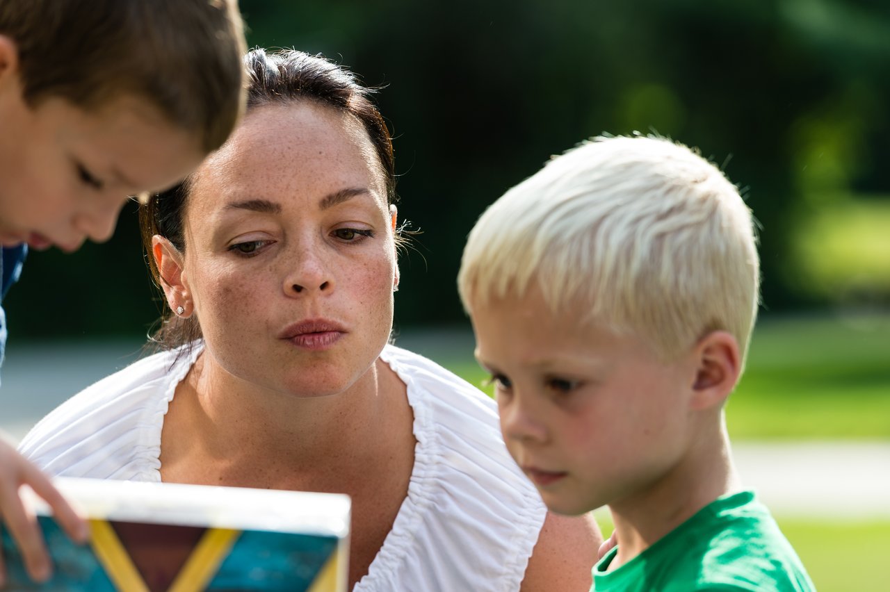 A woman and two children look at a colorful box during an outdoor birthday party.
