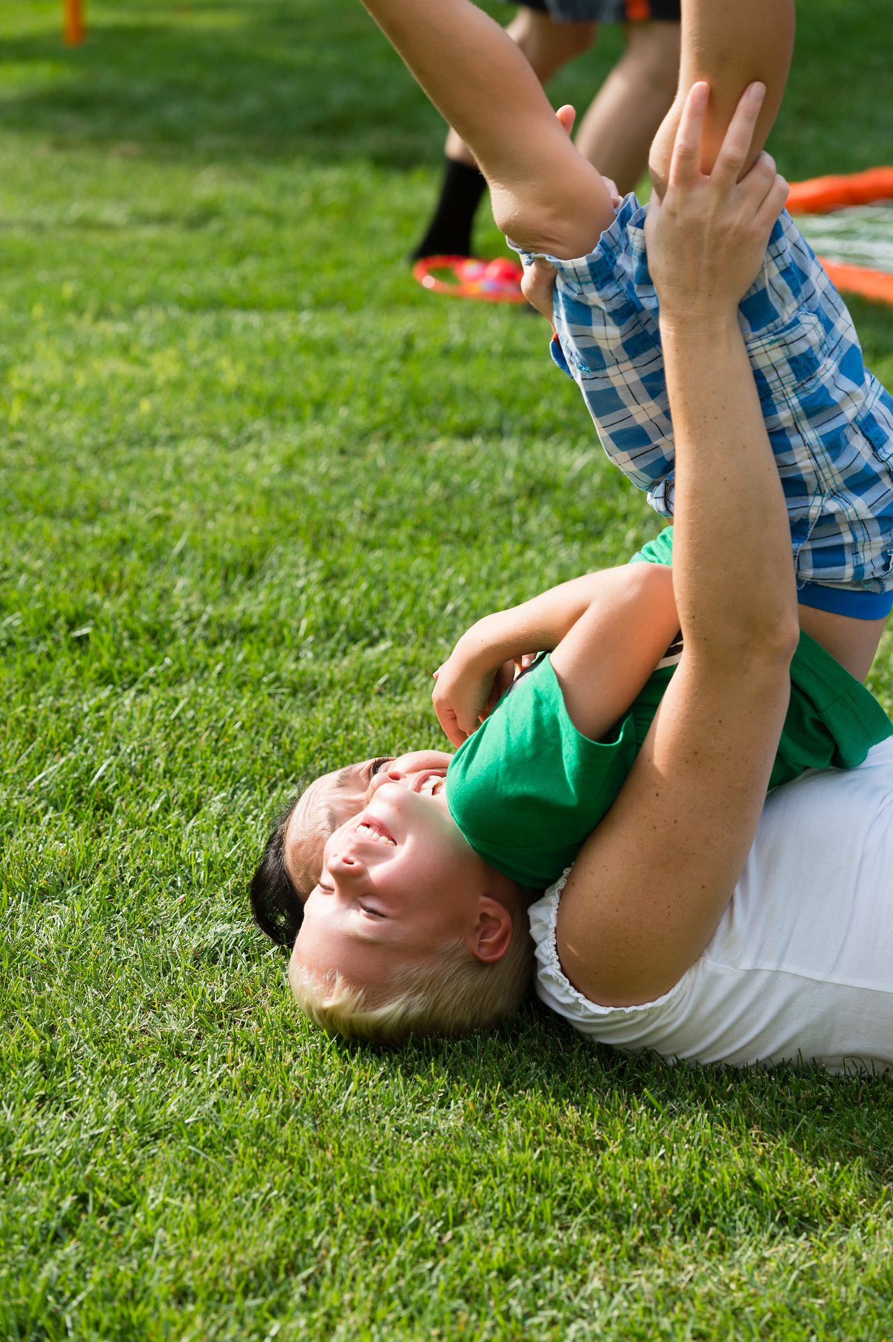 A child and an adult playfully wrestle on the grass, both laughing and enjoying the moment.