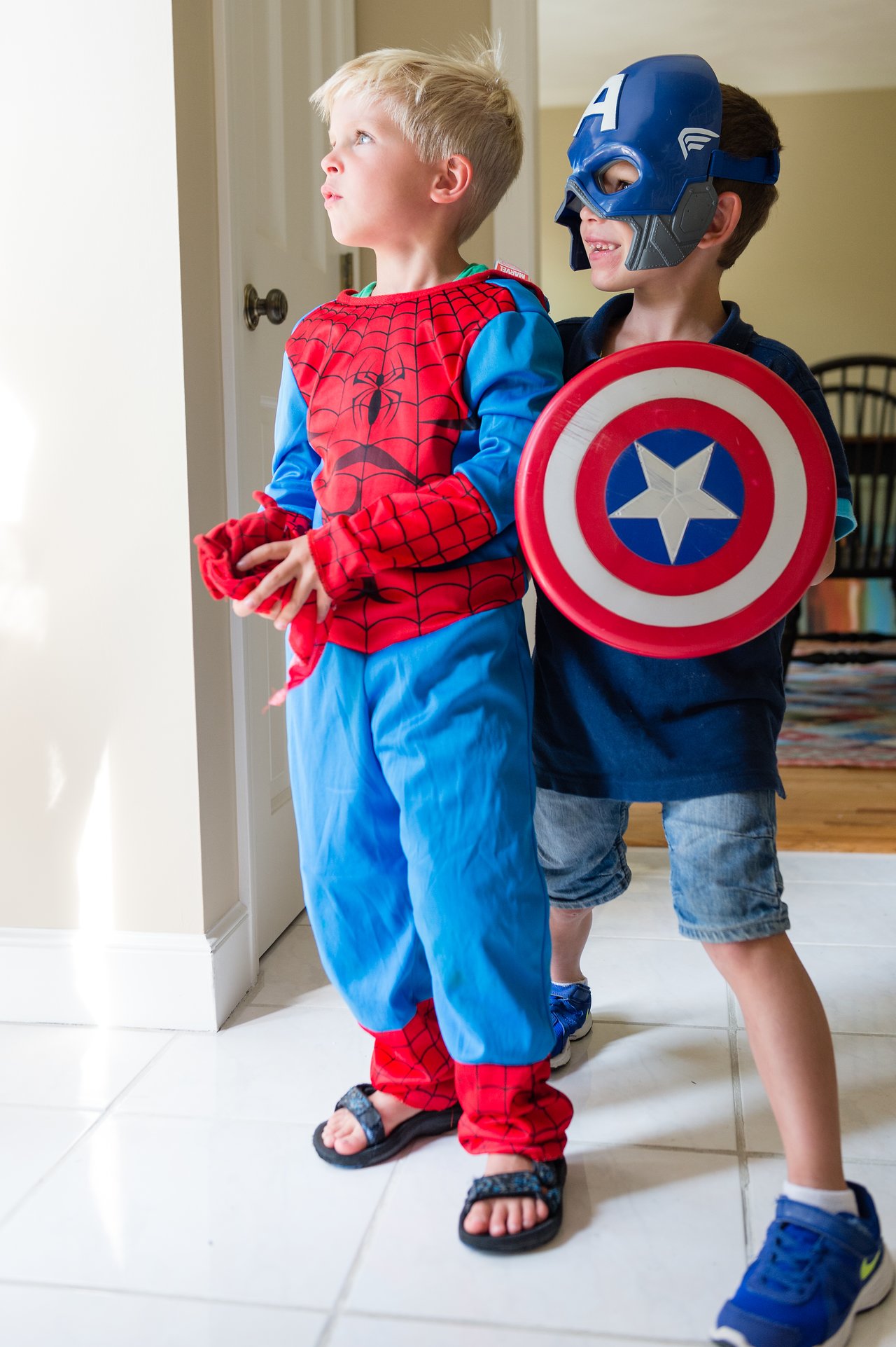 Two children dressed as Spider-Man and Captain America stand together, looking ahead with excitement at a birthday party.
