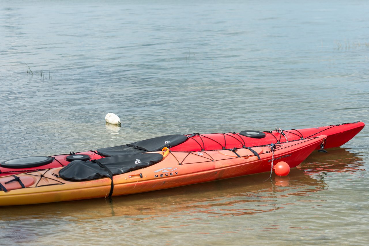 Two red and orange kayaks rest in shallow, calm water near a buoy.