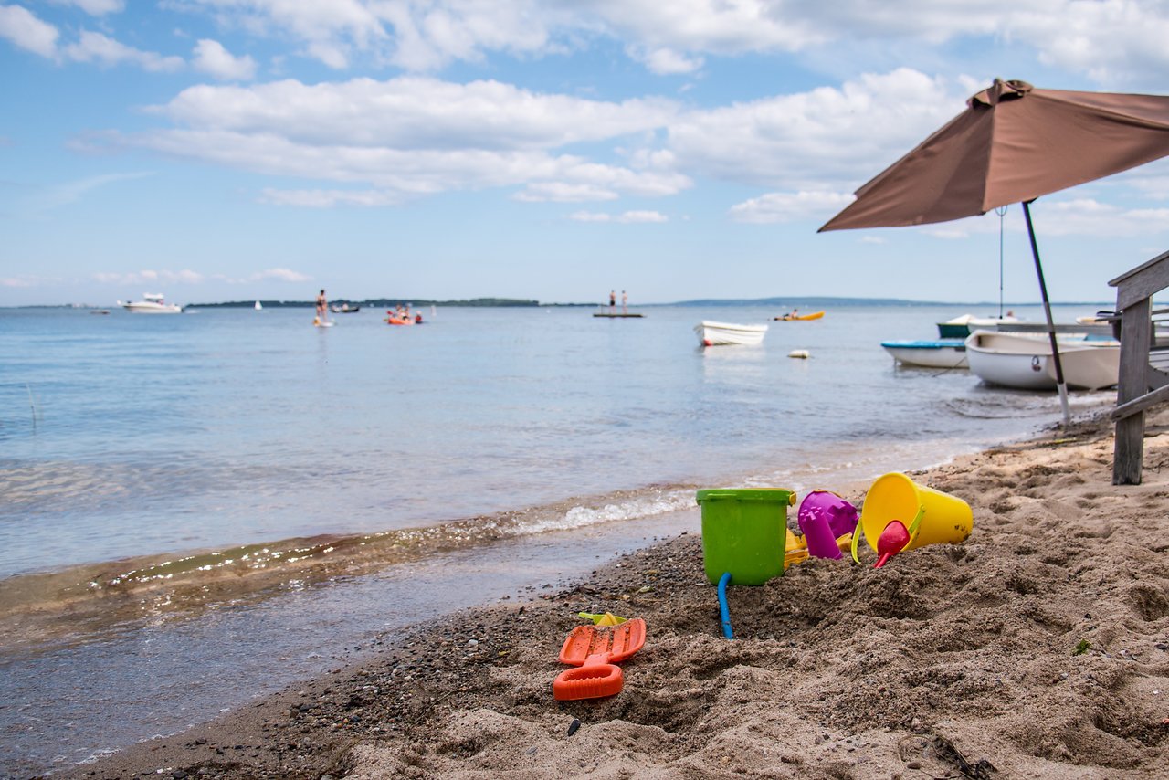 Colorful sand toys on a sandy beach with boats in the water and people enjoying the ocean.