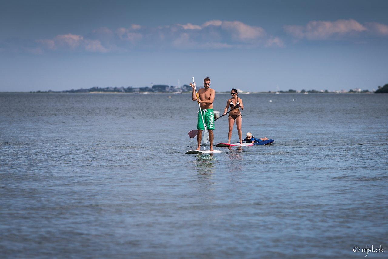 A man and woman paddleboarding on calm water, with a child lying on a small board nearby.