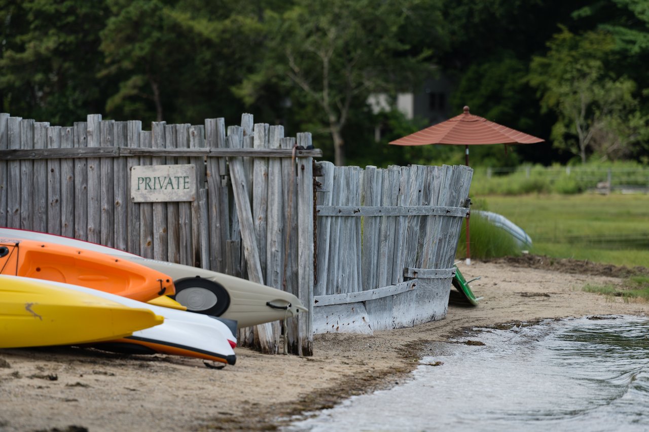 Several kayaks rest on a sandy shore near a weathered wooden fence with a "Private" sign.