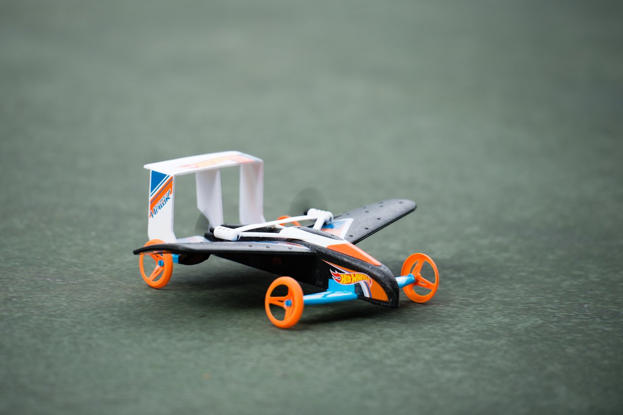 A small toy car with wings and orange wheels sits on a green surface.