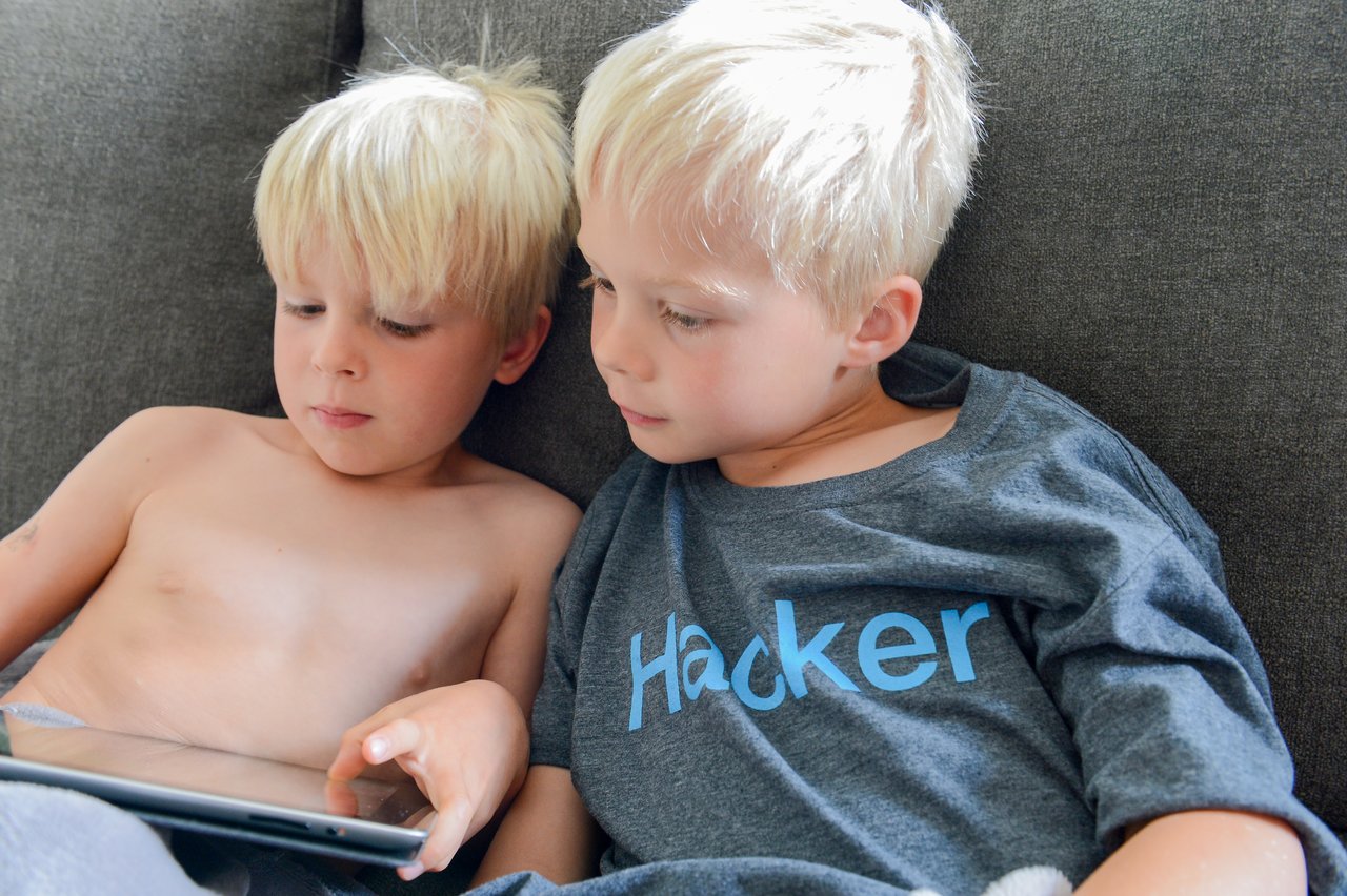 Two young boys sit on a couch, focused on a tablet.