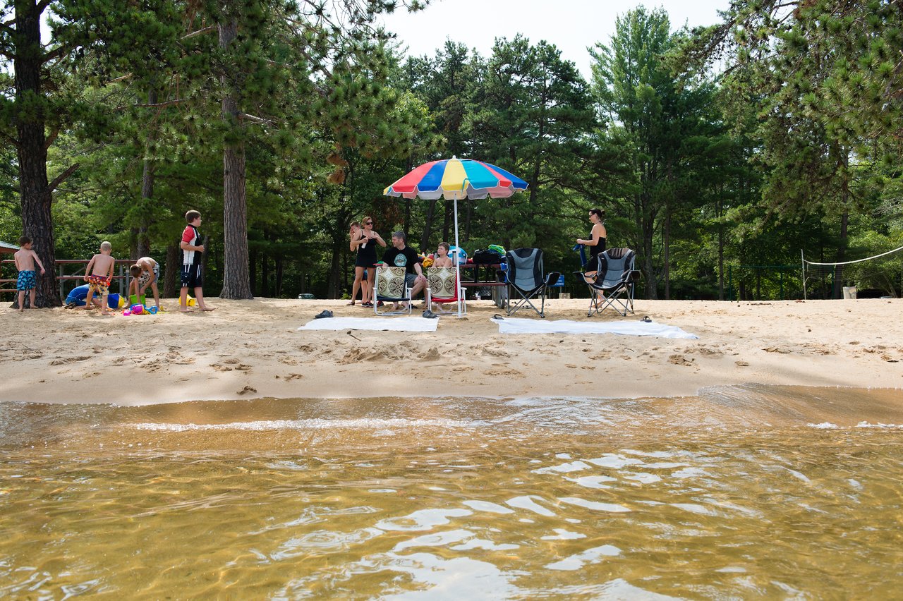 People relax on a sandy beach with chairs and an umbrella, while children play near the water.