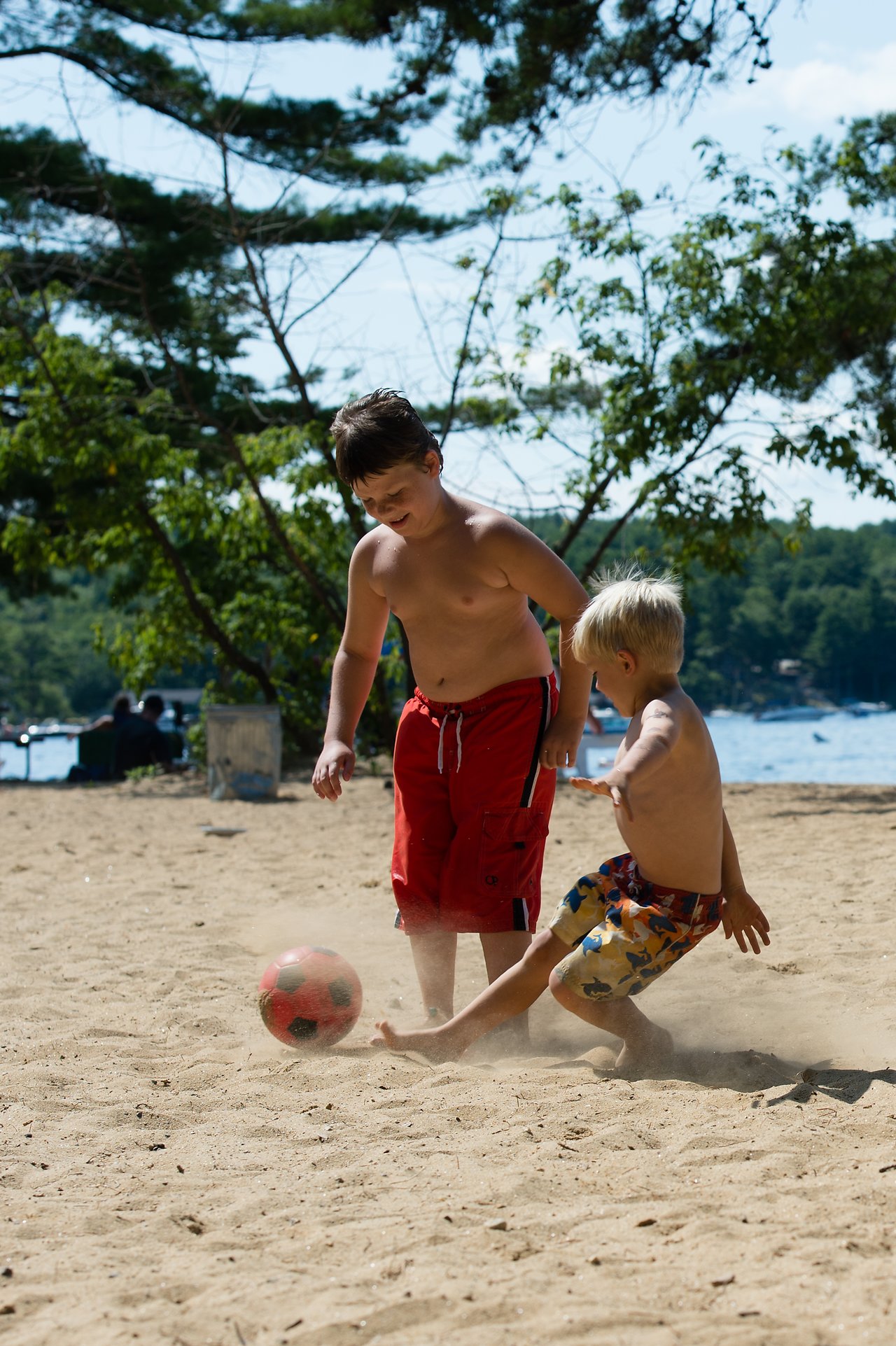 Two boys play soccer on a sandy beach, kicking up dust as they compete for the ball.
